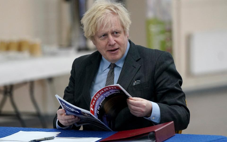 Boris Johnson reads a magazine as he visits a COVID-19 vaccination centre in Batley, - AP Pool