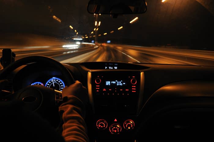 View from inside a moving car at night, showing the dashboard, speedometer, and blurred road lights outside the windshield