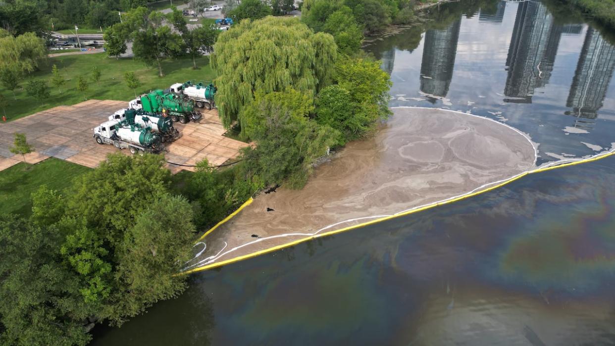 A drone view of the runoff from an industrial fire in Mimico Creek. There is a pond of beige sludge the size of a city pool that crews are trying to clean up. The Humber Bay Park west parking lot and boat ramp are closed and heavy machinery has been brought in. (Patrick Morrell/CBC News - image credit)