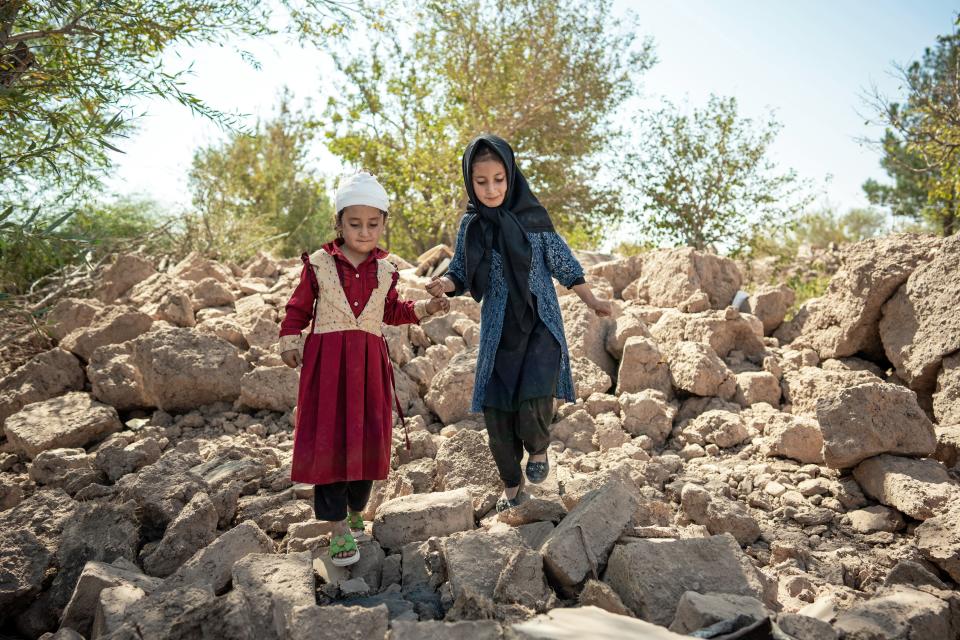 Six-year-old Marzwa (left) walks with her sister, Elina, in the remains of her village wearing a red dress - one of her few possessions that was not buried under the earthquake in Karnil Wardaka village, Zinda Jan District, western Afghanistan.