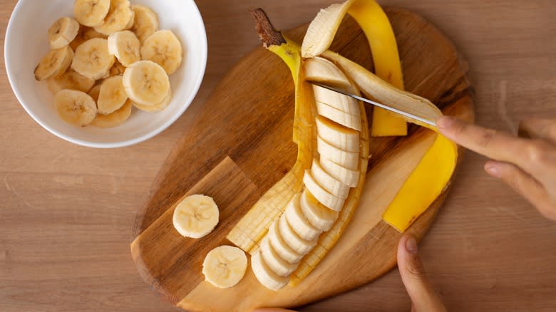 Top-down view of a hand slicing bananas on a cutting board