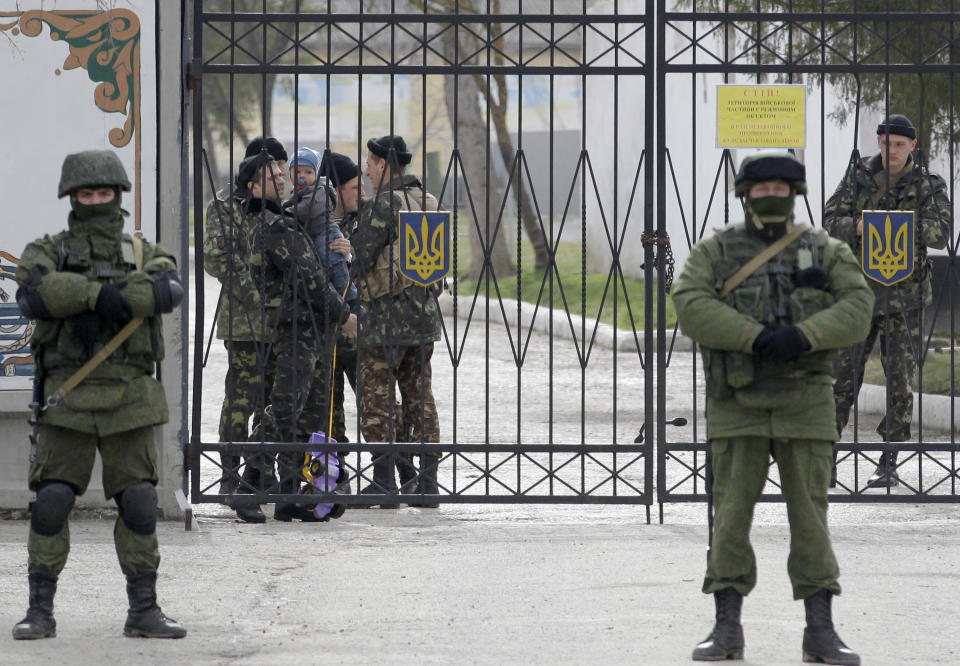 A Ukrainian soldier with a childm 2nd left, watches Russian soldier guard the gate of an infantry base in Perevalne, Ukraine, Tuesday, March 4, 2014. Russian President Vladimir Putin said Moscow reserves the right to use all means to protect Russians in Ukraine as U.S. Secretary of State John Kerry was on his way to Kiev. Tensions remained high in the strategic Ukrainian peninsula of Crimea with troops loyal to Moscow firing warning shots to ward off protesting Ukrainian soldiers. (AP Photo/Darko Vojinovic)