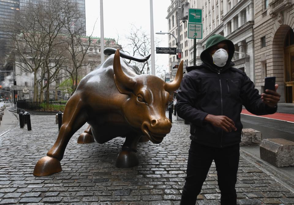 A man wearing a face mask takes a selfie at the Charging Bull statue on March 23, 2020  near the New Stock Exchange in New York City. - Wall Street fell early March 23, 2020 as Congress wrangled over a massive stimulus package while the Federal Reserve unveiled new emergency programs to boost the economy including with unlimited bond buying. About 45 minutes into trading, the Dow Jones Industrial Average was down 0.6 percent at 19,053.17, and the broad-based S&amp;P 500 also fell 0.6 percent to 2,290.31 after regaining some ground lost just after the open. (Photo by Angela Weiss / AFP) (Photo by ANGELA WEISS/AFP via Getty Images)