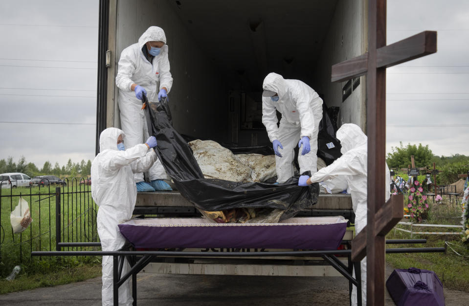 Workers take from a refrigerator truck and put into a coffin a body of unidentified civilian murdered by the Russian troops during Russian occupation in Bucha, on the outskirts of Kyiv, Ukraine, Thursday, Aug. 11, 2022. Eleven unidentified bodies exhumed from a mass grave were buried in Bucha Thursday.(AP Photo/Efrem Lukatsky)