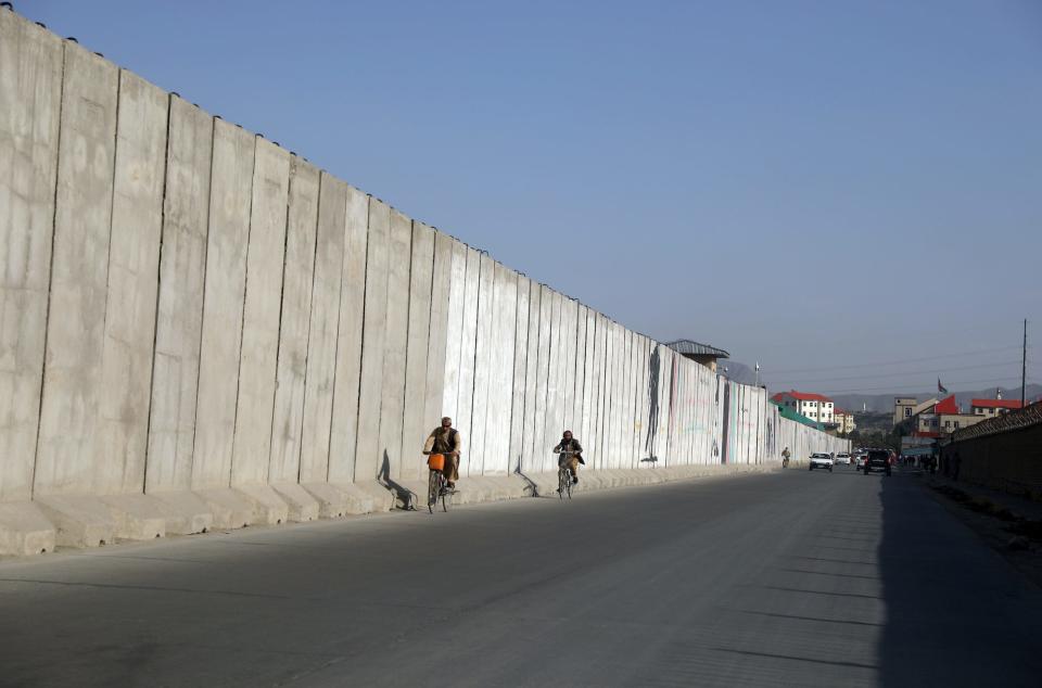 Afghan men ride their bicycles walk past blast walls in Kabul