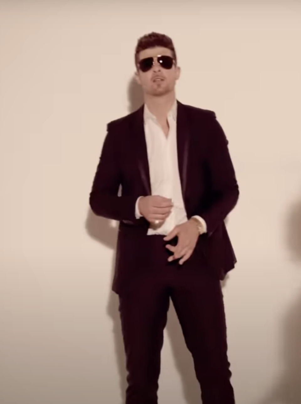 Robin Thicke in dark suit and sunglasses poses against a wall