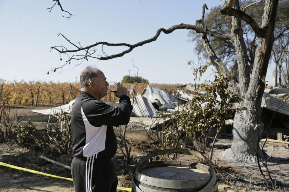 In this Wednesday, Nov. 6, 2019 photo, Izzy Lewkosky, of Kansas City, Kan., tastes a glass of Cabernet Sauvignon while looking out at the wildfire incinerated Soda Rock Winery in Healdsburg, Calif. Despite a late October blaze that raged through one of the world's best-known wine-growing regions. forcing evacuations in two mid-sized towns, wine production in Sonoma County escaped largely unscathed. (AP Photo/Eric Risberg)