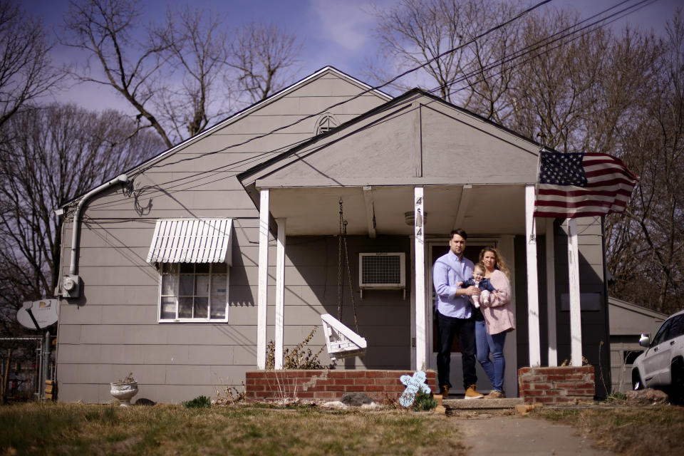 Logan DeWitt with his wife Mckenzie and daughter Elizabeth stand outside their home Monday, March 8, 2021, in Kansas City, Kan. Because he could work at home, Logan kept his job through the pandemic while his wife lost hers and went back to school. Their financial situation was further complicated with the birth of their daughter nine months ago. (AP Photo/Charlie Riedel)