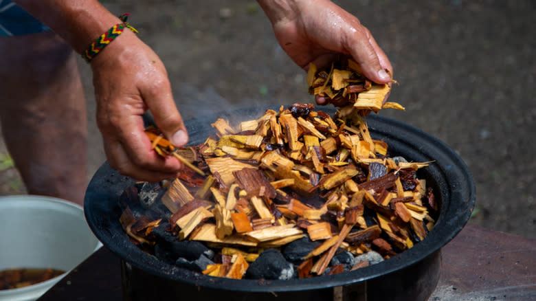 Hands putting wood chips on hot coals