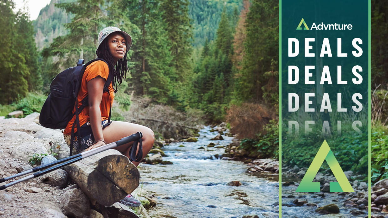  Woman with trekking poles pausing by stream 