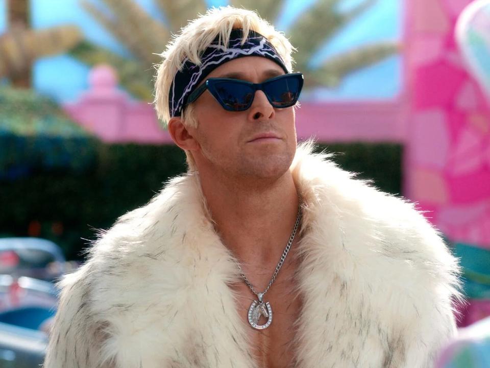 Ryan Gosling is dressed as Ken in black sunglasses, a bandana, and a white fur coat as part of a scene of the "Barbie" movie.