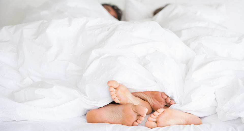 A couple lie in bed with only their feet showing from under the blanket.