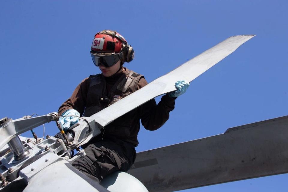 A photo of a mechanic holding a helicopter rotor and scrubbing the blade.