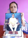 Anindita Mitra, 61, poses with a portrait of her husband late Narayan Mitra, at her house in Silchar, India, Sunday, Sept. 13, 2020. Narayan Mitra, wasn't listed among those killed by the coronavirus that authorities put out daily because the test results confirming COVID-19 arrived after his death. In India, people who die with other preexisting conditions are often not counted as COVID-19 deaths, while only those who test positive for the virus before dying are included in the official tally in many states. (AP Photo/Joy Roy)