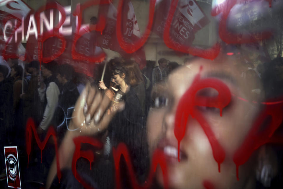 Protesters are reflected in a billboard during a demonstration in Lyon, central France, Wednesday, March 15, 2023. Opponents of French President Emmanuel Macron's pension plan are staging a new round of strikes and protests as a joint committee of senators and lower-house lawmakers examines the contested bill. (AP Photo/Laurent Cipriani)