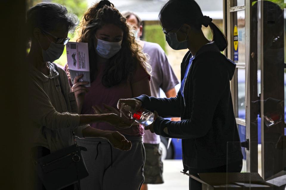 Polling clerk Diana Lee, right, makes sure every person entering uses hand sanitizer