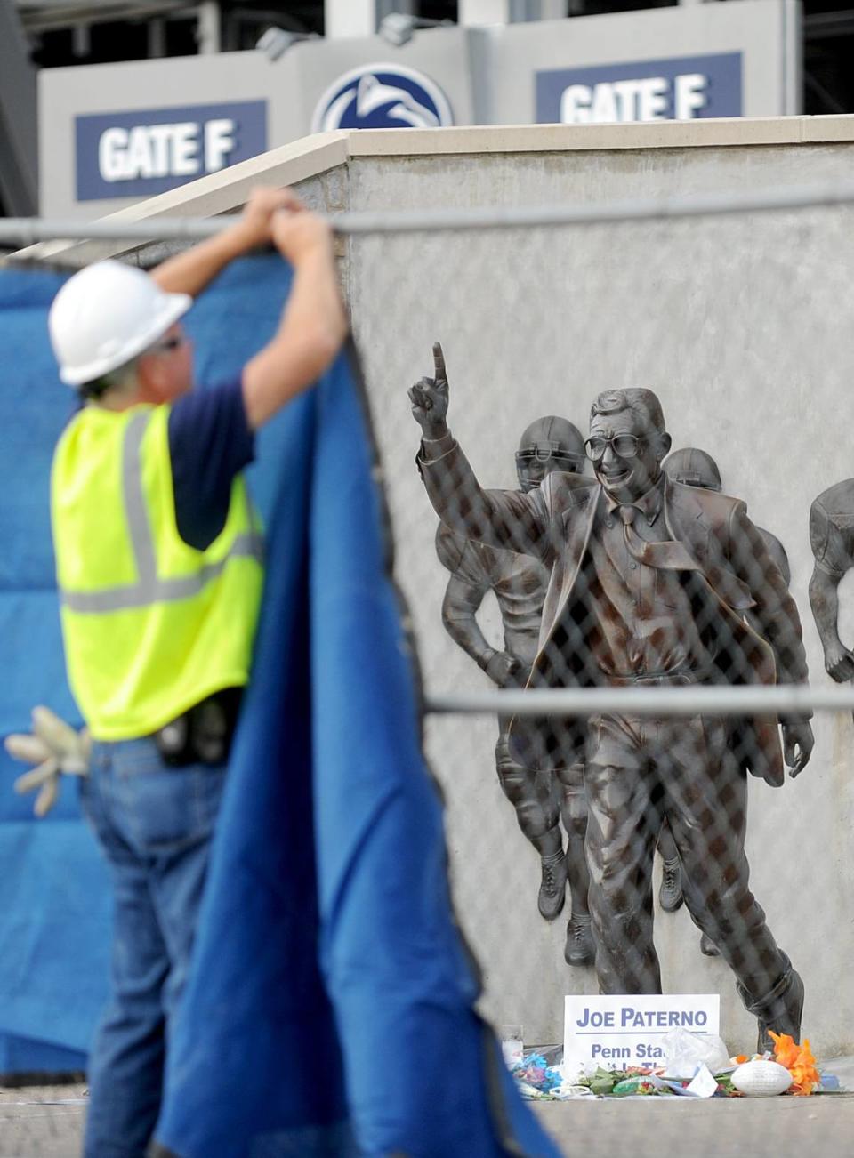 A worker hangs a blue tarp over the fence that was put up around the Joe Paterno statue as crews worked to remove the statue in the early hours of Sunday, July 22, 2012.