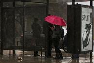 Commuters take cover from the rain at a bus stop in Los Angeles, Friday, Jan. 20, 2017. The second in a trio of storms has arrived in California. Rain, heavy at times, is overspreading the state early Friday and a flash flood warning has been issued for southeastern Sonoma County. Storm warnings are posted up and down the Sierra Nevada and across the mountains of Southern California. (AP Photo/Damian Dovarganes)