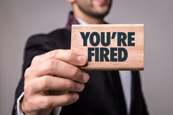 Man holding wooden block that says You're Fired in black letters.