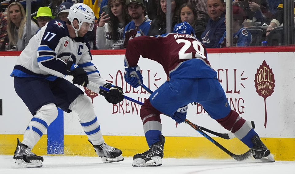 Winnipeg Jets center Adam Lowry, left, and Colorado Avalanche center Nathan MacKinnon dig for the puck during the second period of Game 3 of an NHL hockey Stanley Cup first-round playoff series Friday, April 26, 2024, in Denver. (AP Photo/David Zalubowski)