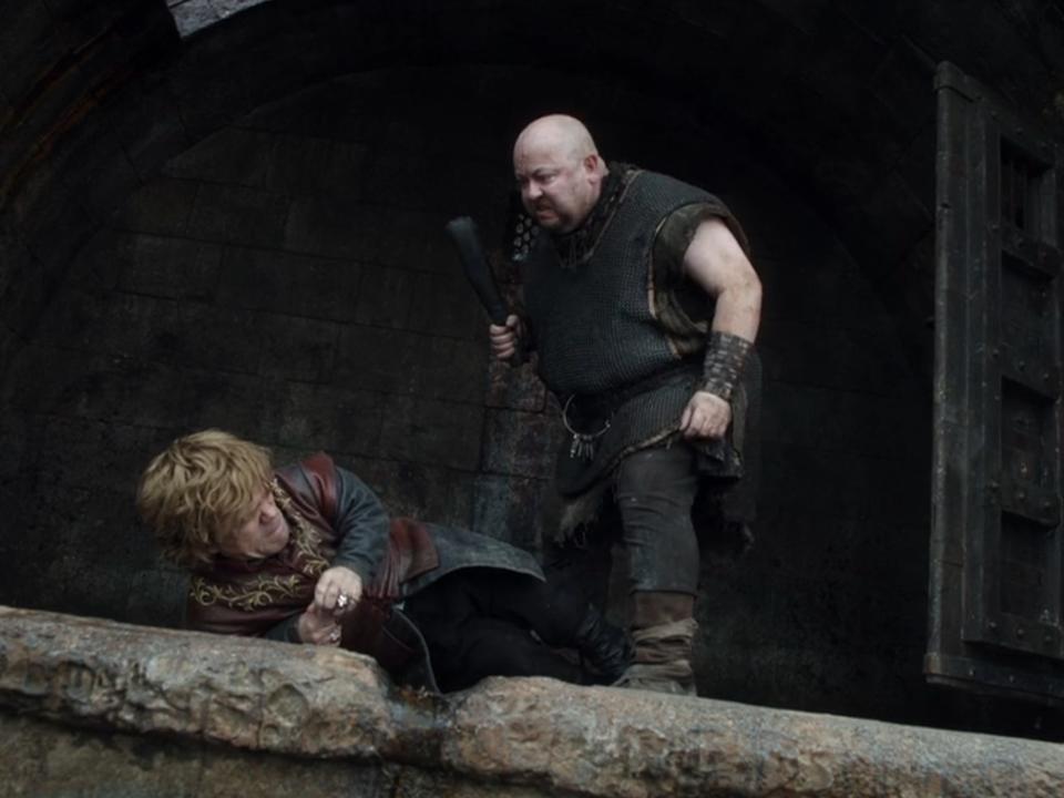 mord the jailer, a large man with a bald head and face scar, looming over tyrion lanister as he cowers on the edge of a cell