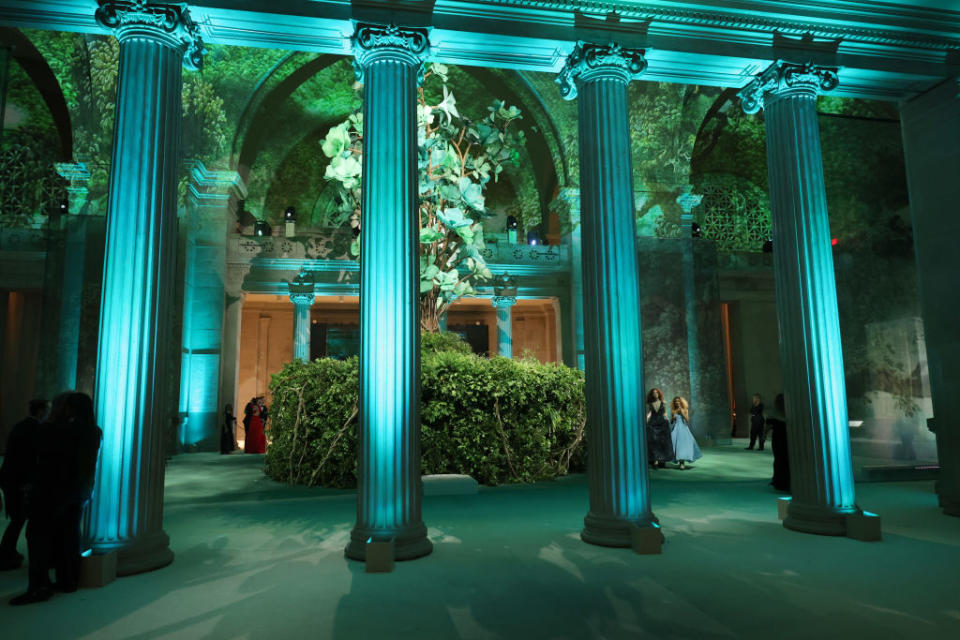 A lavish event space with illuminated columns, lush greenery, and attendees in formal attire