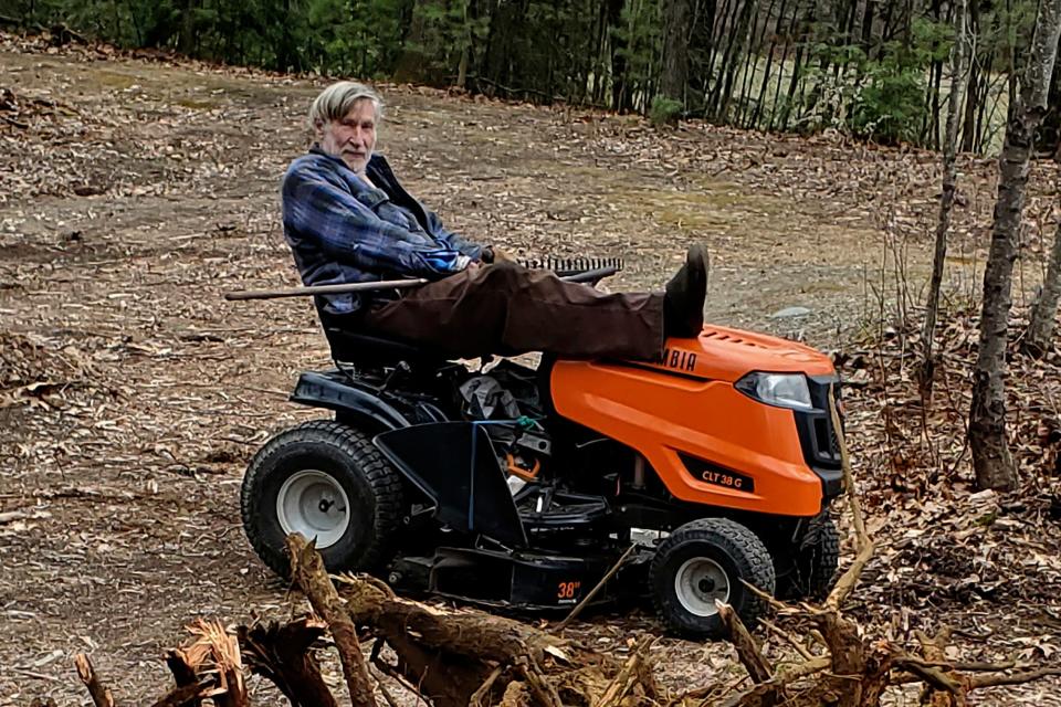 In this photo provided by Ed Smith, Geoffrey Holt rests his leg on top of his riding mower in Hinsdale, N.H., on April 4, 2020. Holt left the town of Hinsdale nearly $4 million when he died last June.