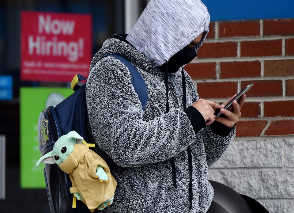 A man wearing a face mask stands next to a "Now Hiring " sign in front of a store on December 18, 2020, in Arlington, Virginia . - US lawmakers were hammering out final details on a major coronavirus relief package and an attached federal funding bill but sticking points could push them past a midnight deadline, threatening a government shutdown amid swelling health and fiscal crises. Without an agreement, millions of unemployed workers will lose their special pandemic benefits before the end of the year, and an eviction moratorium is set to lapse within days. (Photo by Olivier DOULIERY / AFP) (Photo by OLIVIER DOULIERY/AFP via Getty Images)