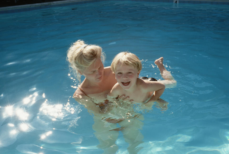 Woman and child playing in a pool. The woman holds the smiling child above water