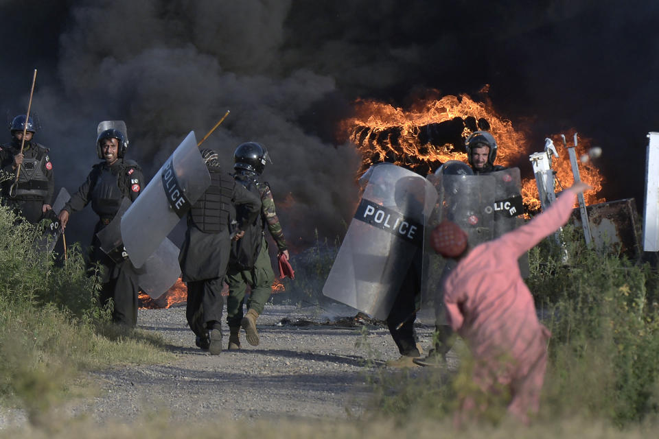 A supporter of Pakistan's former Prime Minister Imran Khan throws a stone towards police officers after they set fire to a pile of tires during clashes, in Islamabad, Pakistan, Wednesday, May 10, 2023. Khan appeared in court Wednesday, a day after he was dragged from another court and arrested in Islamabad, and his supporters clashed with police across the country. A judge was asked to approve keeping the 70-year-old opposition leader in custody for up to 14 days. (AP Photo)