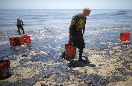 William McConnaughey, 56, (R) who drove from San Diego to volunteer, carries buckets of oil from an oil slick in bare feet along the coast of Refugio State Beach in Goleta, California, United States, May 20, 2015. REUTERS/Lucy Nicholson