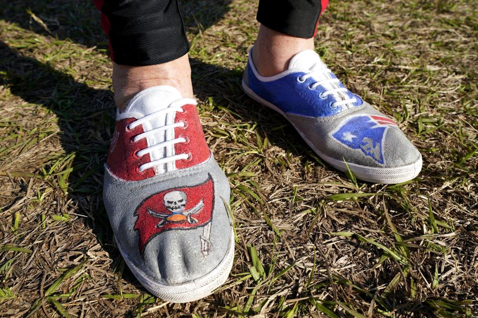 FILE - A fan arrives wearing shoes from both Tampa Bay Buccaneers quarterback Tom Brady's teams before the NFL Super Bowl 55 football game between the Kansas City Chiefs and Tampa Bay Buccaneers in Tampa, Fla., in this Sunday, Feb. 7, 2021, file photo. Brady hasn't played an NFL football game in New England since Jan. 4, 2020. But remnants from his 20-year run with the Patriots remain everywhere in Foxborough. With Brady's new Tampa home just as rabid about the player who brought it a championship in Year 1, it's created a tug-of-war between the fan bases as he gets set to return to the place where his career began. (AP Photo/Mark Humphrey, File)