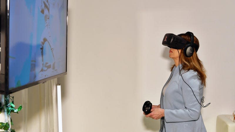 A woman wearing a Oculus Quest VR headset holding controllers and looking at a screen.