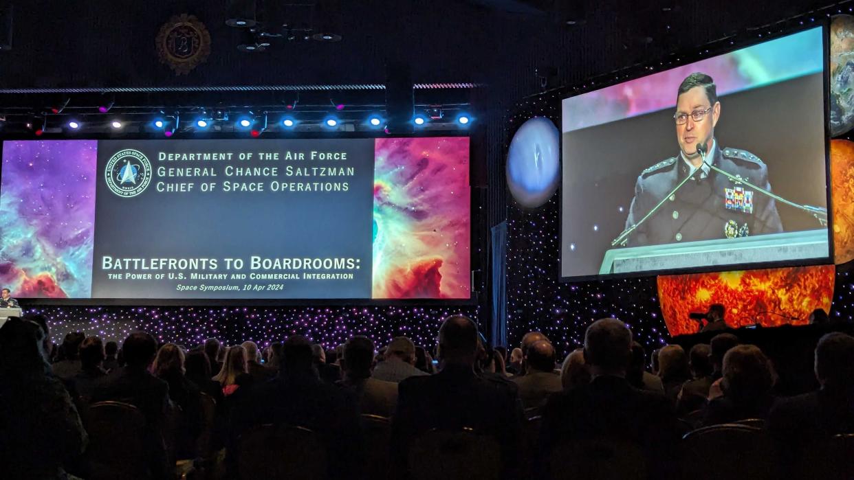  A man in a black military dress outfit gives a speech on a stage decorated with illuminated stars and planets. 