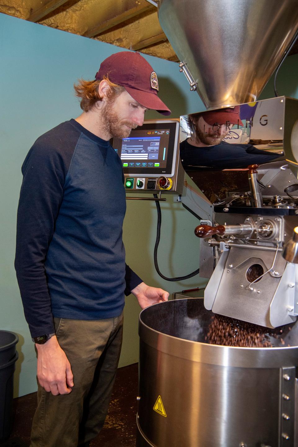 Matthew McDaniel, green coffee buyer and lead roaster at Cooperative Coffee Roasters, watches as freshly roasted beans fall from the roaster in West Asheville, January 19, 2024.
