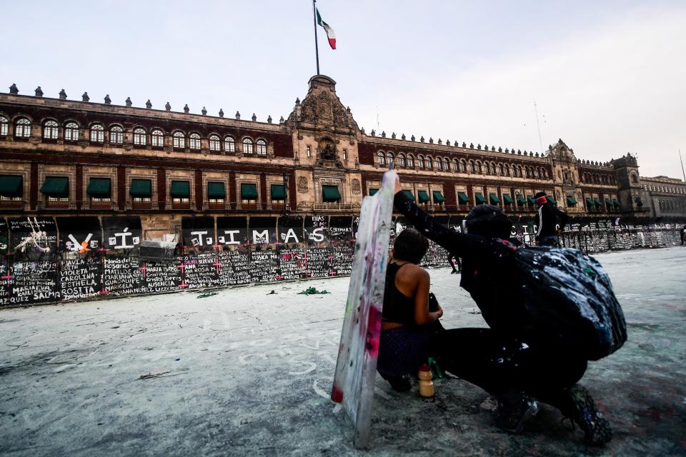 Women take cover as they clash with the police, behind a fence in front of the National Palace, as they protest during a demonstration to commemorate the International Women's Day  in Mexico City, on March 8, 2021. (Photo by PEDRO PARDO / AFP) (Photo by PEDRO PARDO/AFP via Getty Images)