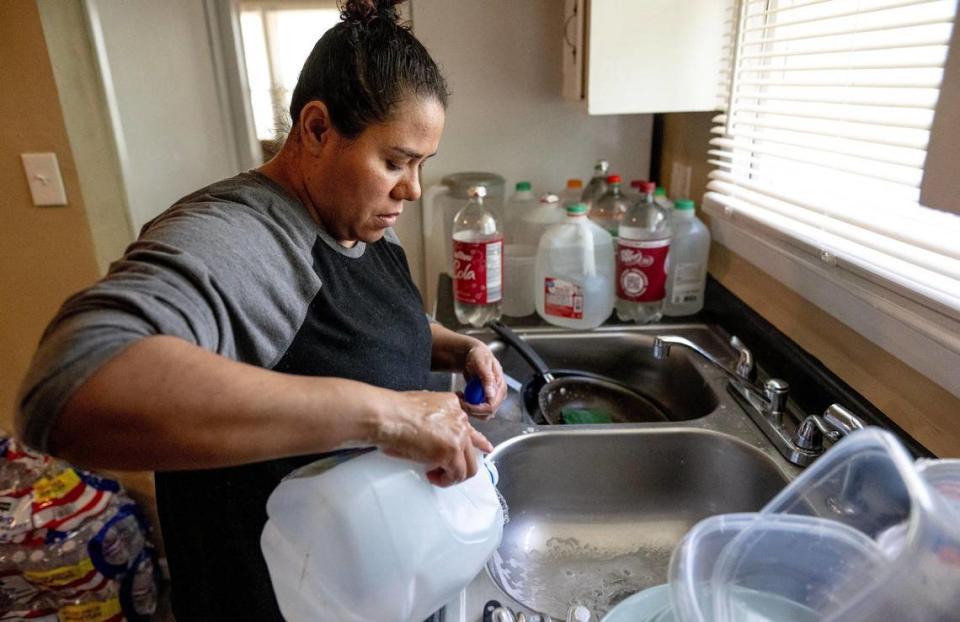 Jessica Martínez enjuaga el jabón del fregadero de la cocina de su casa, el viernes 26 de mayo de 2023, en Kansas City. Debido a un saldo pendiente dejado por un inquilino anterior, KC Water cortó el agua a la casa de Martínez en abril. Desde entonces, la familia ha tenido que ser creativa para sus necesidades de agua, incluyendo el transportar en auto botes de basura llenos de agua a su casa.