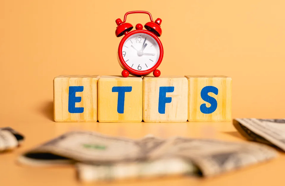 The word ETFS from Exchange Traded Funds written in English language on wooden cubes. An alarm clock and dollar bills in the composition. Economy and investment concepts.