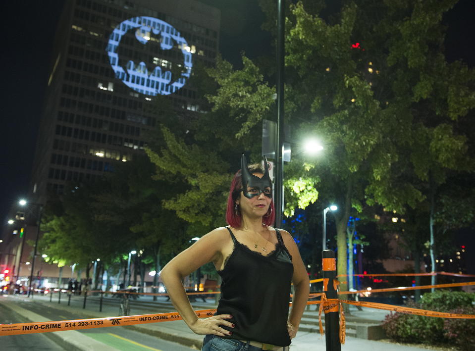 A woman poses for a photo beneath a Batman signal projected onto a building to celebrate Batman Day in Montreal, Saturday, Sept. 21, 2019. The night sky all over the world is lighting up Saturday with an illumination of the famed bat insignia to mark a special anniversary for Batman. DC Comics is carrying off a celebration of Batman Day to mark the 80th anniversary of the appearance of crimefighter Bruce Wayne and his masked hidden identity. (Graham Hughes/The Canadian Press via AP)