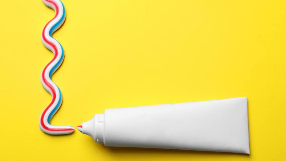 Blank tube with squeezed out toothpaste on yellow background, flat lay. Space for text