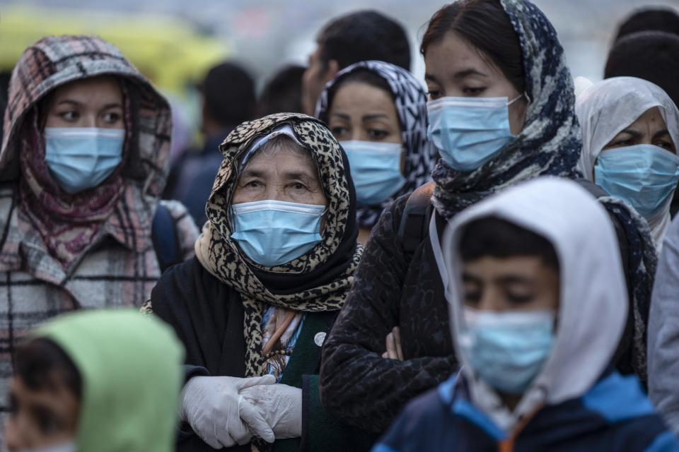 FILE - In this Monday, May 4, 2020 file photo, refugees and migrants wearing masks to prevent the spread of the new coronavirus, wait to get on a bus after their arrival at the port of Piraeus, near Athens. A Washington-based Syrian rights group filed on Thursday, Jan. 28, 2021 a case with the International Criminal Court calling for an investigation into alleged crimes against humanity by Greece for its treatment of refugees at its borders and in sprawling camps. (AP Photo/Petros Giannakouris, File)