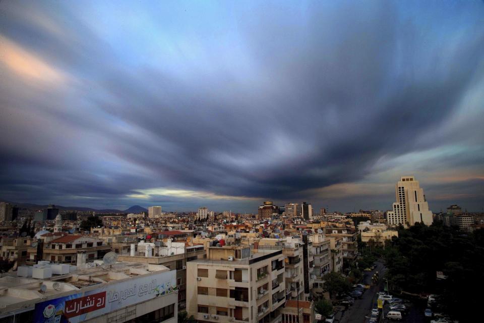 FILE - In this April 12, 2016 file picture taken with a slow shutter speed, clouds hover over the capital city of Damascus, Syria. A new Syrian law empowering the government to confiscate property is threatening to leave refugees stuck in Europe with no homes to return to. (AP Photo/Hassan Ammar, file)