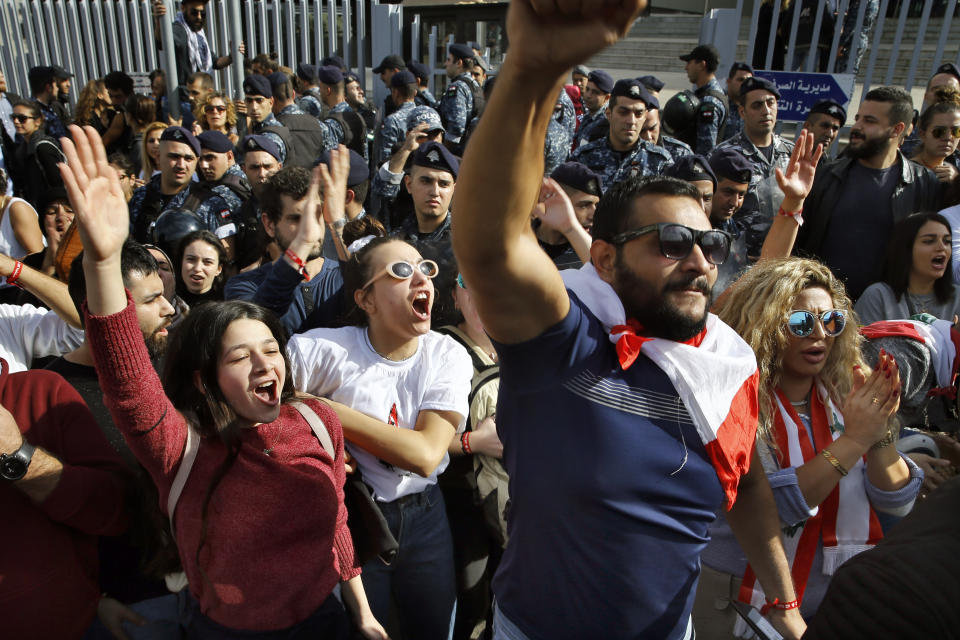 Protesters chant slogans during ongoing protests against the Lebanese political class, as riot police stand guard in front of a Finance Ministry building in Beirut, Lebanon, Friday, Nov. 29, 2019. Protesters have been holding demonstrations since Oct. 17 demanding an end to widespread corruption and mismanagement by the political class that has ruled the country for three decades. (AP Photo/Bilal Hussein)
