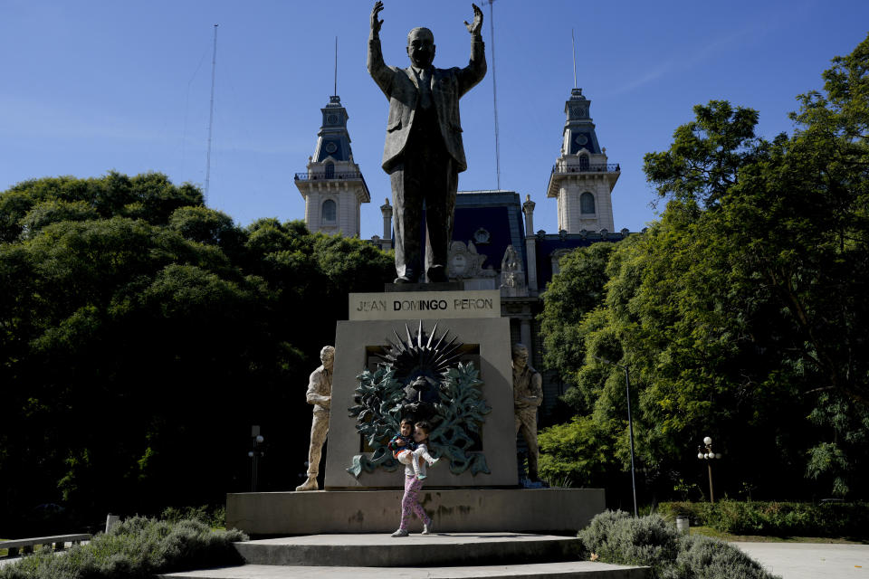 Aksinia Domini, de 6 años, carga a su hermanita Agata, de 3, frente a un monumento dedicado al expresidente argentino Juan Domingo Perón, en un parque en Buenos Aires, Argentina, el sábado 12 de abril de 2023. Los padres de las niñas son parte de un creciente número de personas rusas de la comunidad LGBTQ+ que abandonaron Rusia para establecerse en Argentina tras escapar de la discriminación y la guerra en Ucrania. (AP Foto/Natacha Pisarenko)