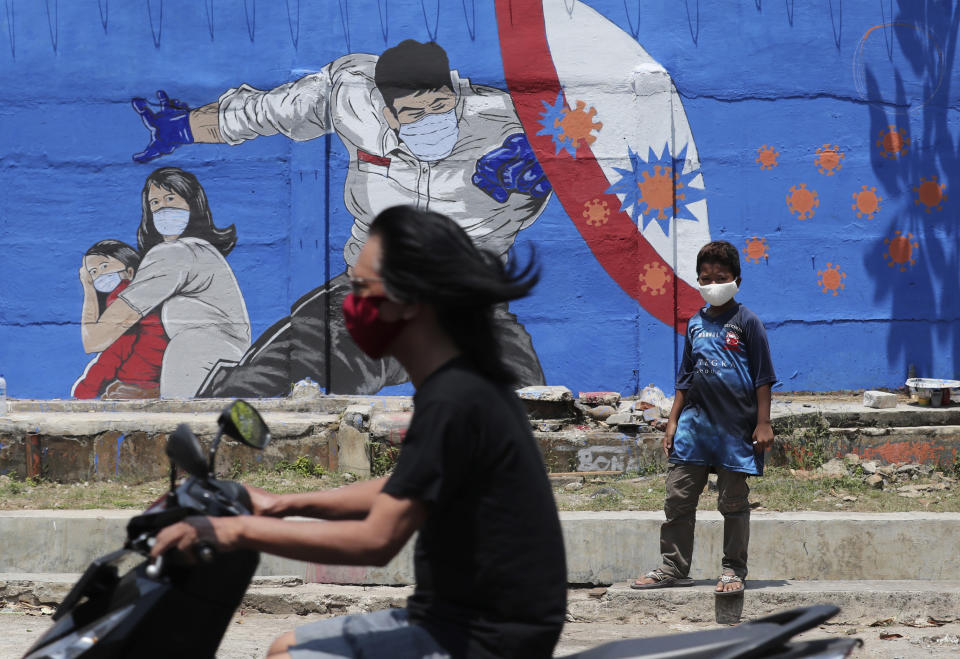 A young boy stands near a coronavirus-themed mural as a motorist rides past by in Jakarta, Indonesia, Thursday, Aug. 27, 2020. (AP Photo/Tatan Syuflana)