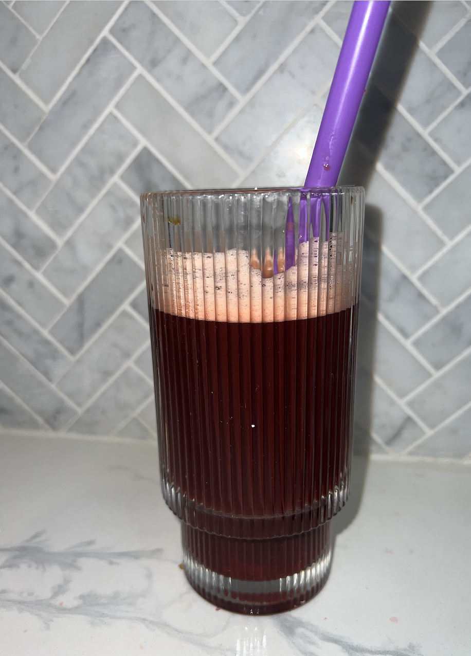 A clear, ribbed glass filled with the dark beverage on the counter