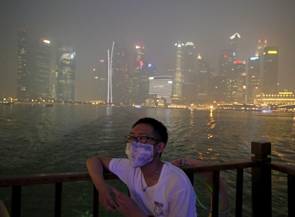 Man wearing a mask watches from a bumboat as he passes the haze-shrouded central business district in Singapore
