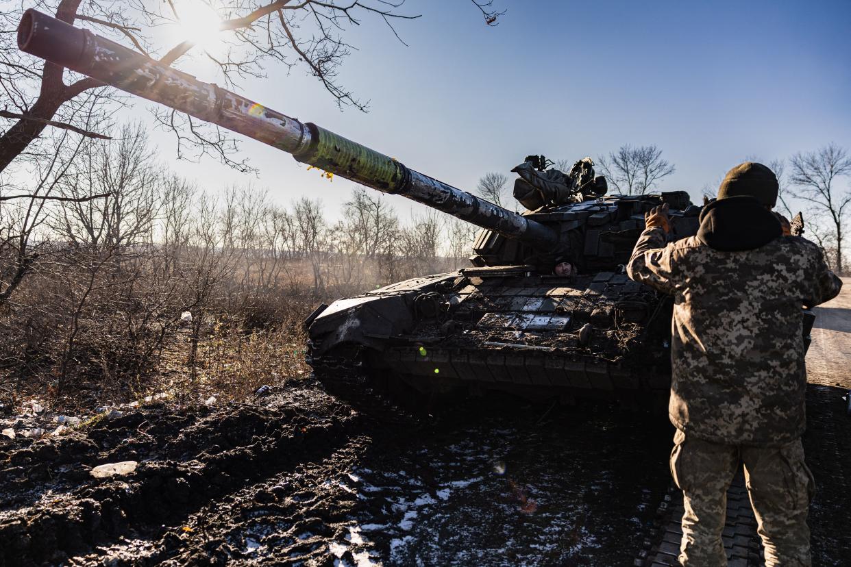 A Ukrainian soldier directs a tank as another drives it forward.