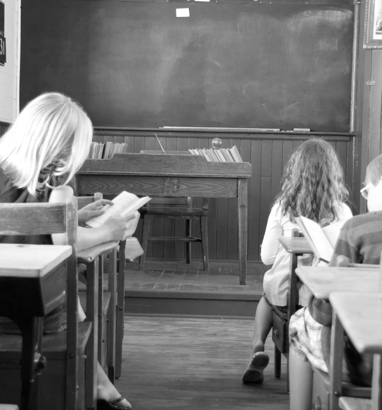 Three children in a vintage classroom reading ... black and white. Copy space on blackboard.