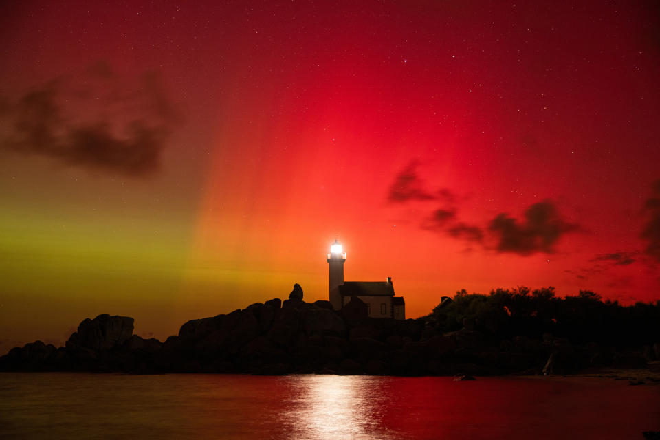 Lighthouse against a dramatic red and green sky at night, with stars and clouds softly visible